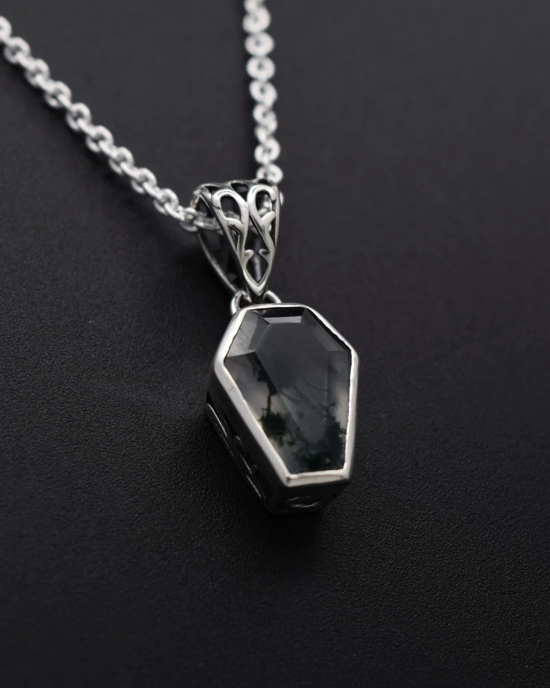 A silver coffin-shaped pendant necklace with a dark, smoky gemstone, displayed on a textured black background.