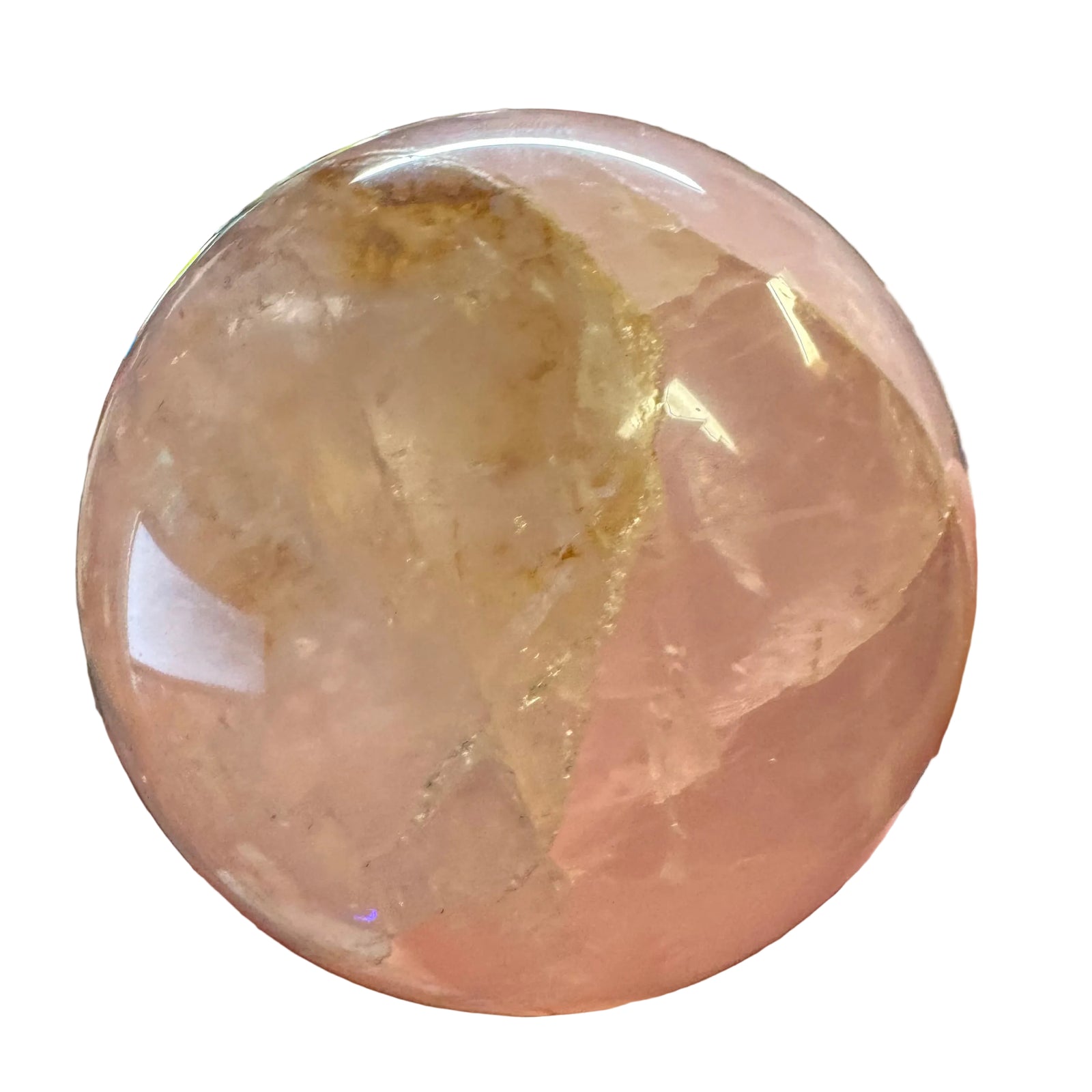 A hand holding a large, polished pink quartz crystal sphere with natural inclusions and cloudy texture, set against a cluttered indoor desk background.