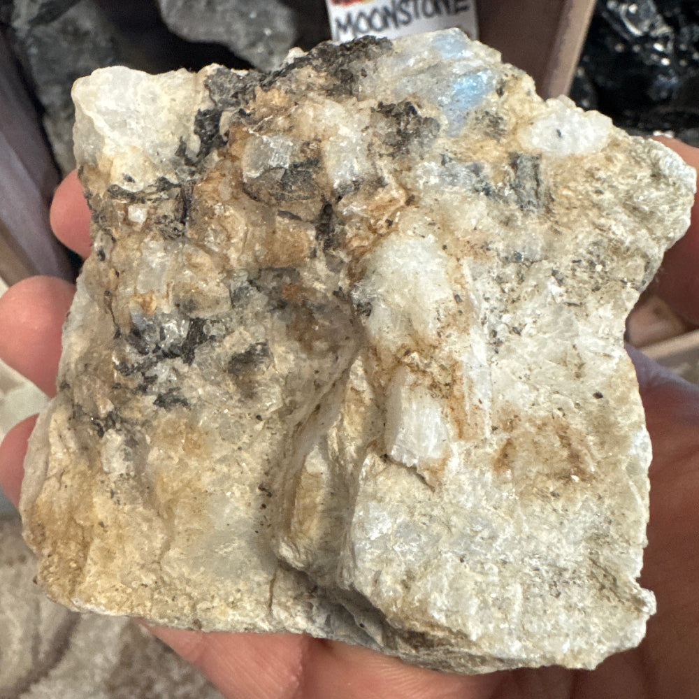 Hand holding a large crystal rock with a visible brand label in the background