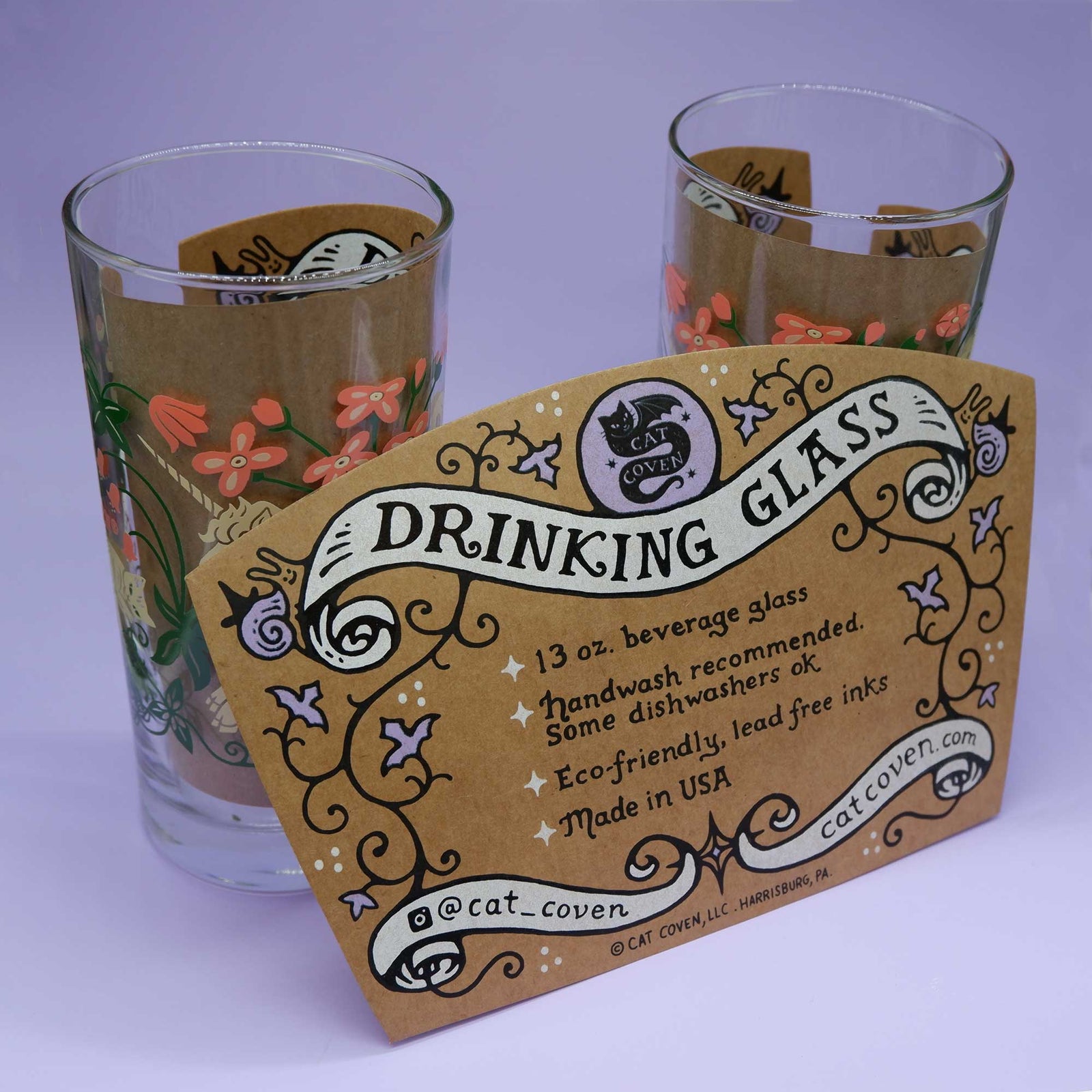 Two glass tumblers with decorative labels on a light purple background