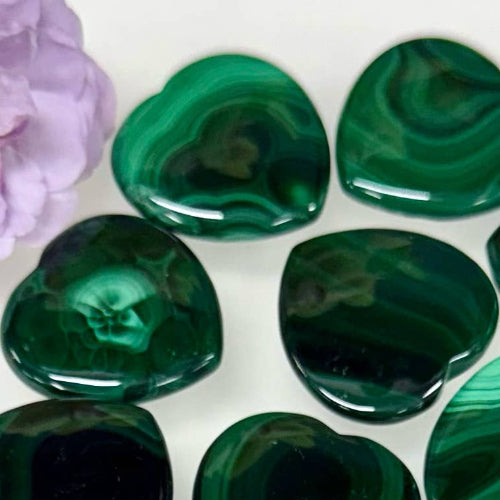Heart-shaped green stones on a white background with a purple flower.