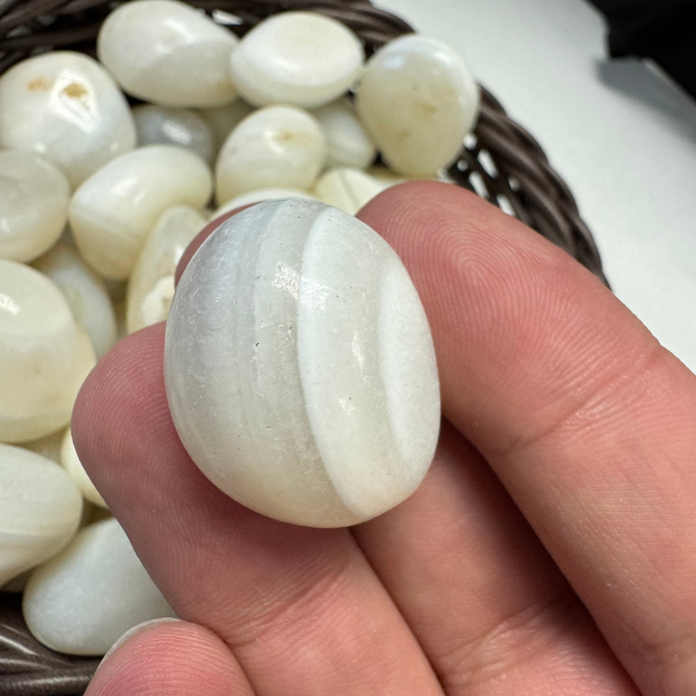 Hand holding a white stone with a woven basket of stones in the background