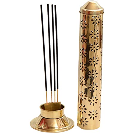 A gold-colored brass incense tower burner with intricate patterns, displayed on a white surface, with various decorative items in the background.