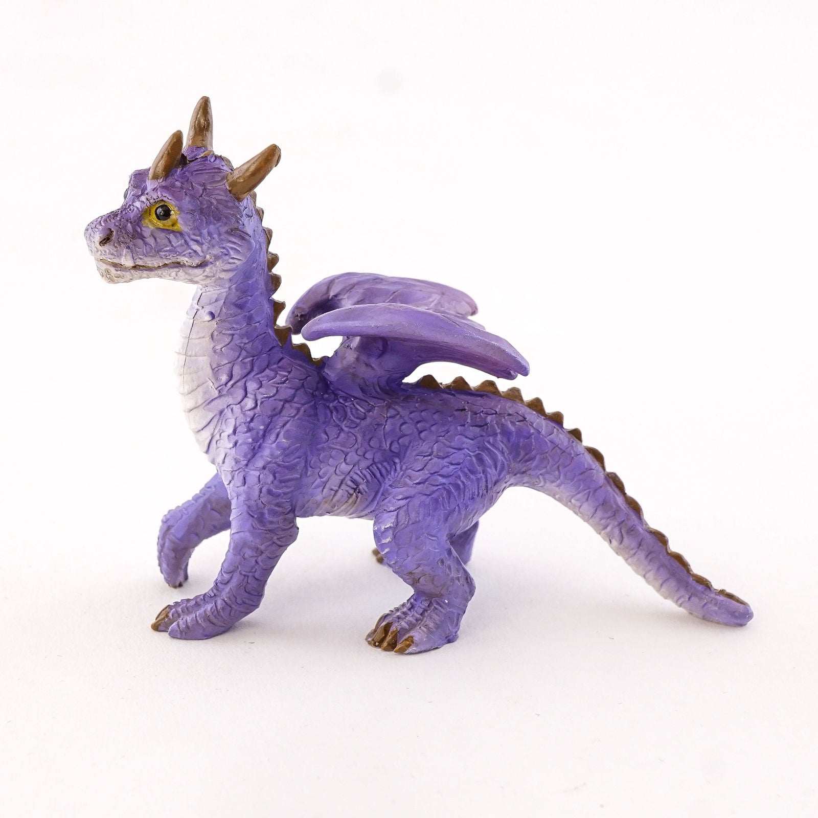It is standing on all fours and has a simultaneously adorable and majestic appearance. He has purple scales and a white underbelly, along with yellow eyes, three horns on its head, and a ridge of spikes down the winged back. It’s a lovely dragon that will be at home anywhere.