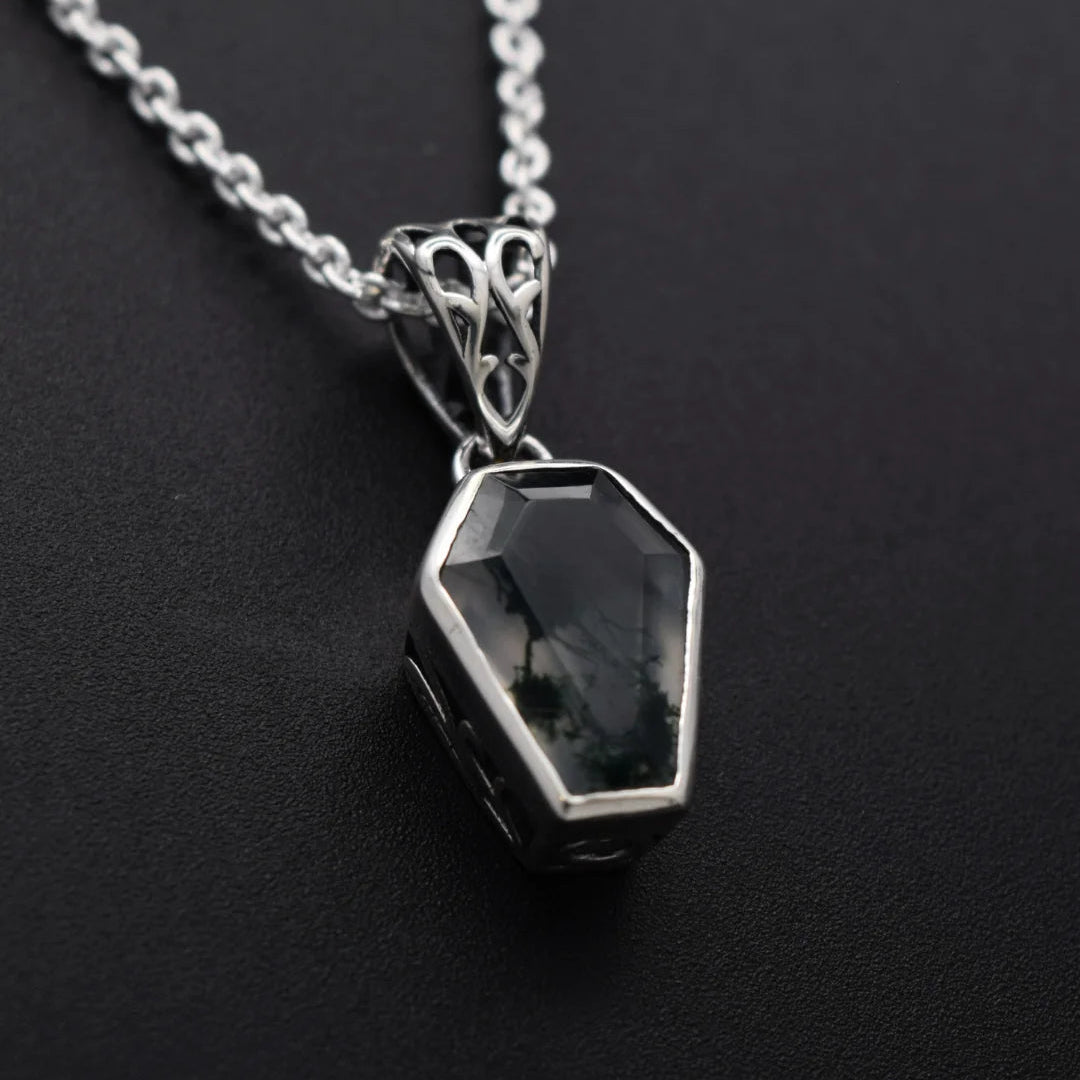 A silver coffin-shaped pendant necklace with a dark, smoky gemstone, displayed on a textured black background.