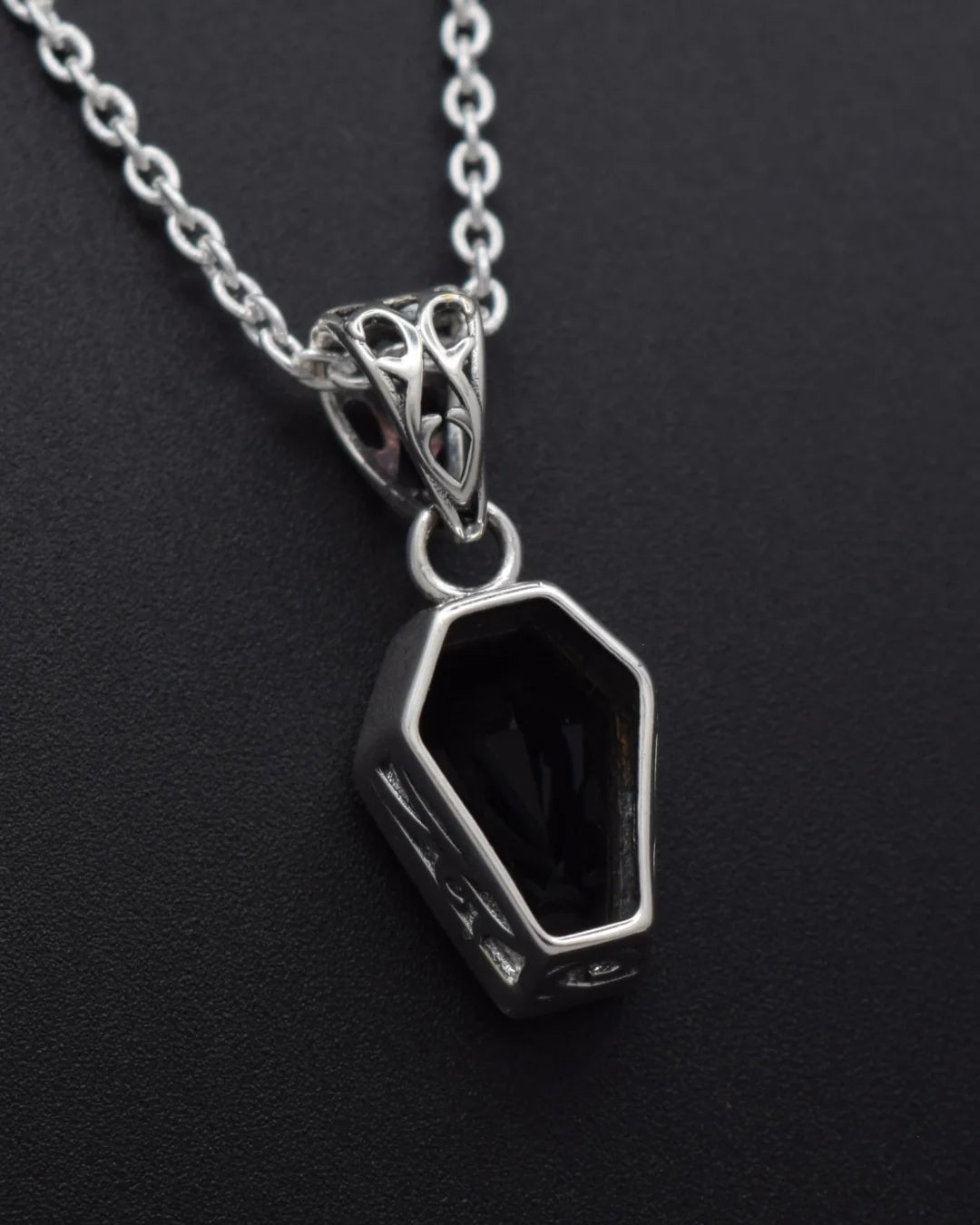 A silver-toned coffin-shaped pendant necklace with a black inlay, shown on a dark textured background.