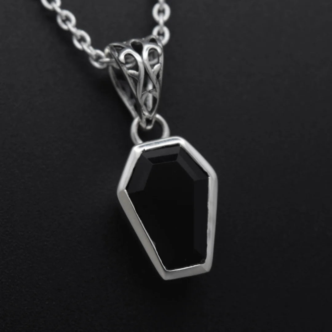 A silver coffin-shaped pendant necklace with a faceted black gemstone, shown on a dark textured background.