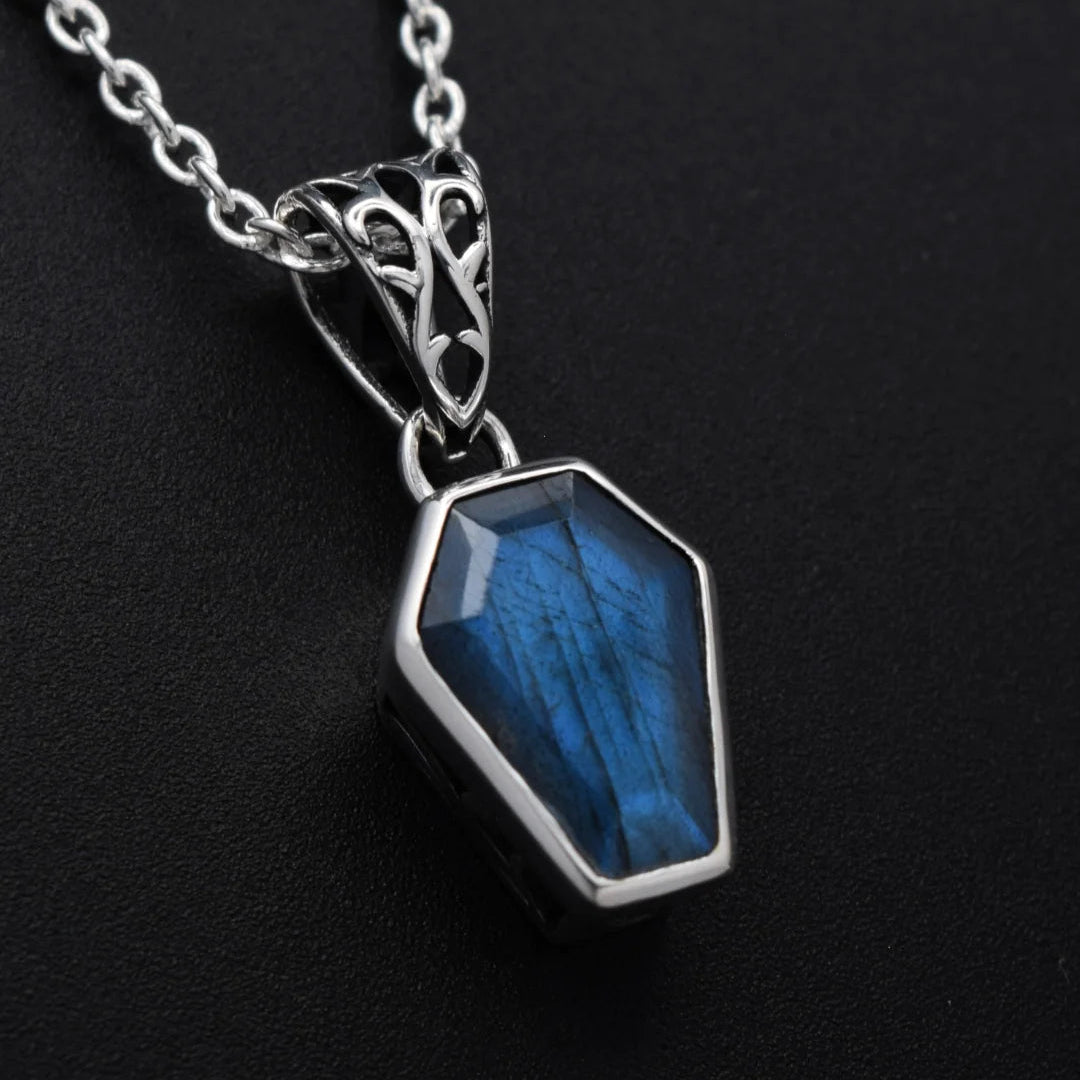A silver pendant necklace featuring a coffin-shaped blue labradorite gemstone, displayed on a dark textured background.