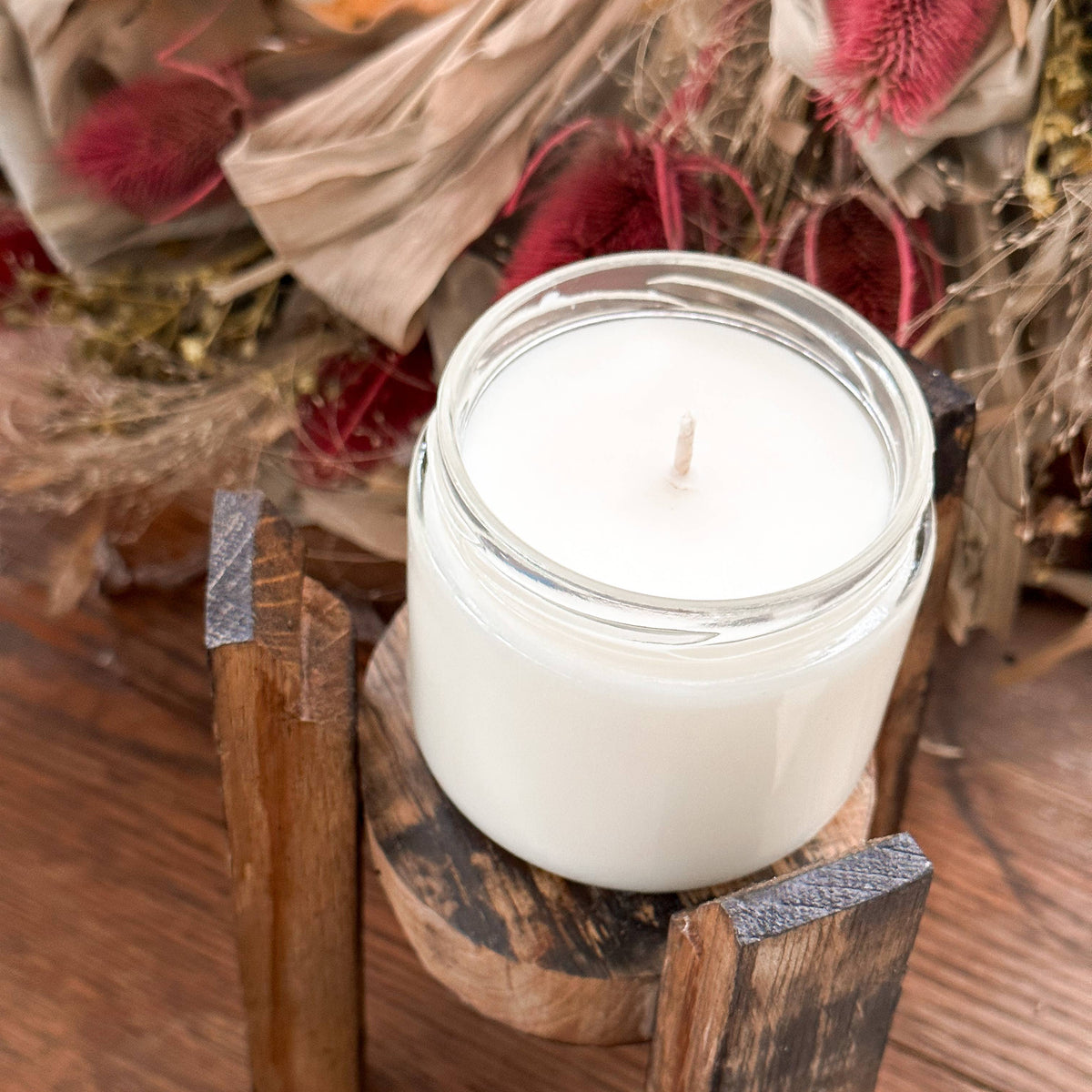 White candle in a rustic wooden holder on a wooden surface with decorative elements.