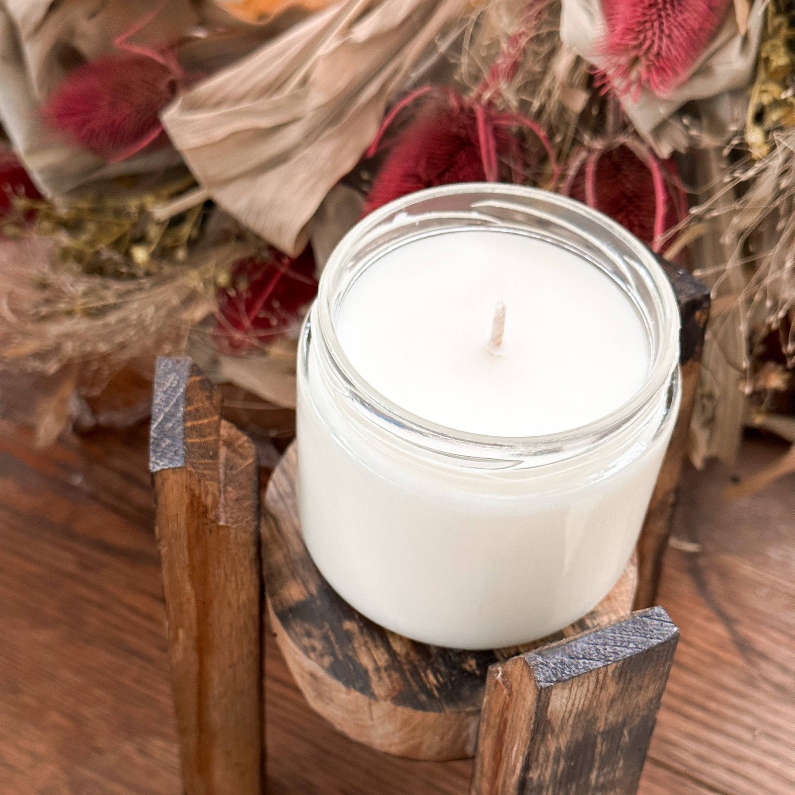 White candle in a rustic wooden holder on a wooden surface with decorative elements.