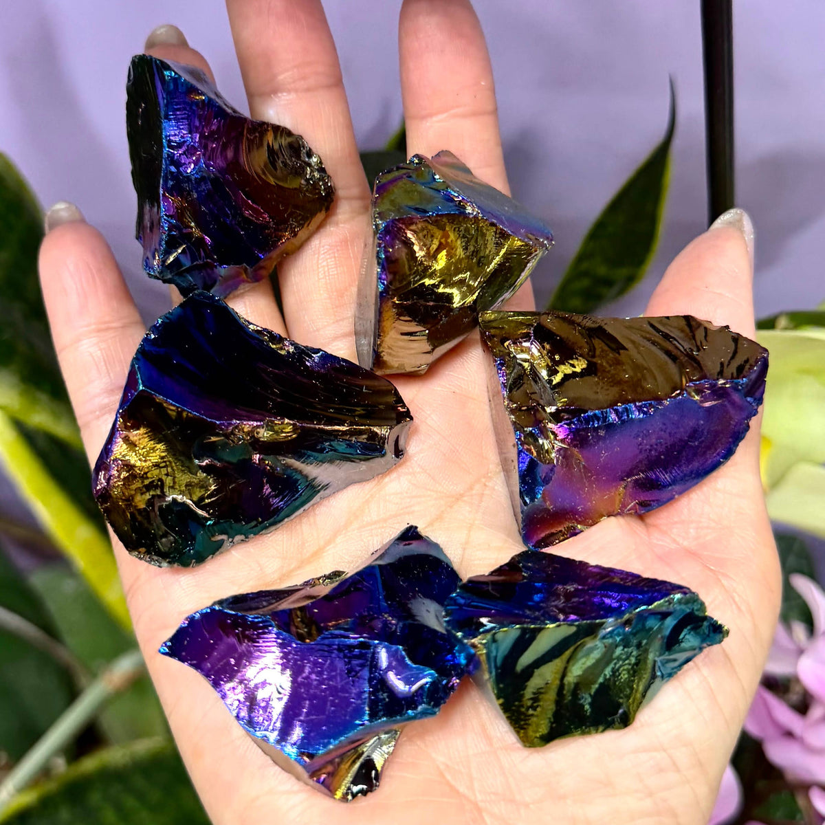 Hand holding iridescent crystal pieces with a blurred natural background
