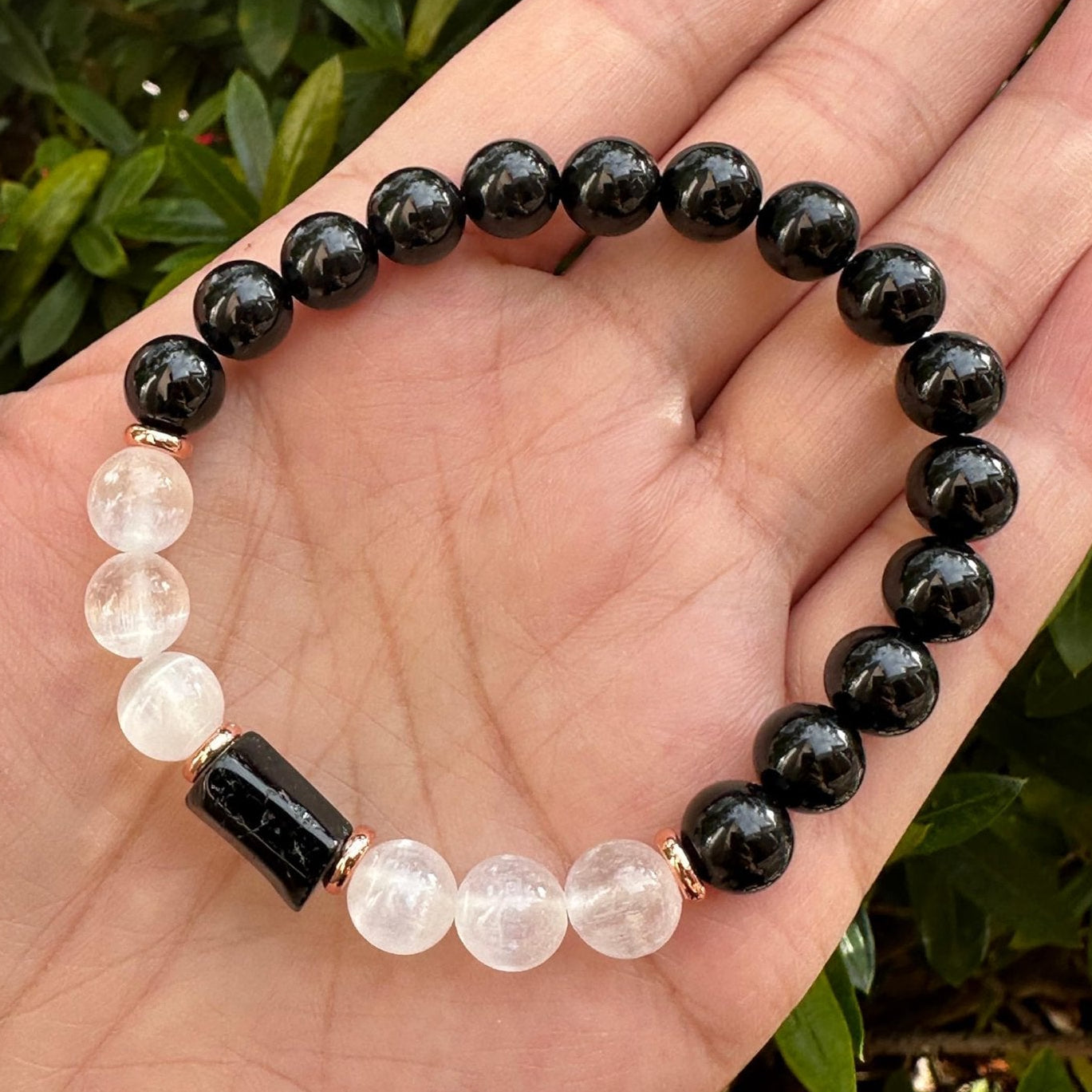 Bracelet with black and white beads held in a hand against a green leafy background