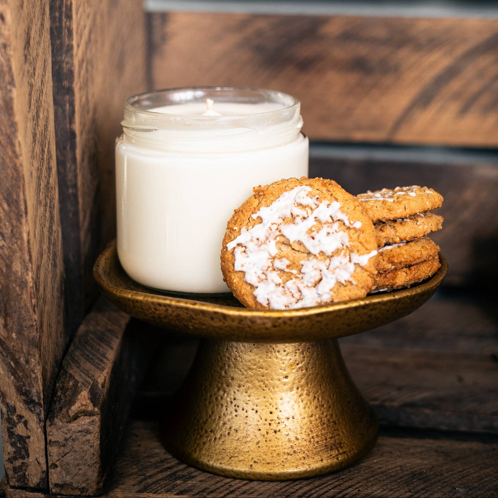 Cookies on a small gold stand next to a candle in a wooden setting