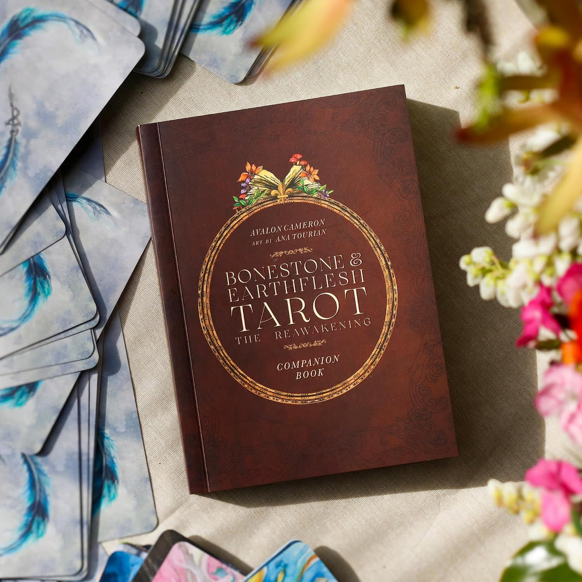 Bonestone & Earthflesh Tarot companion book in brown and gold beside feather-backed cards