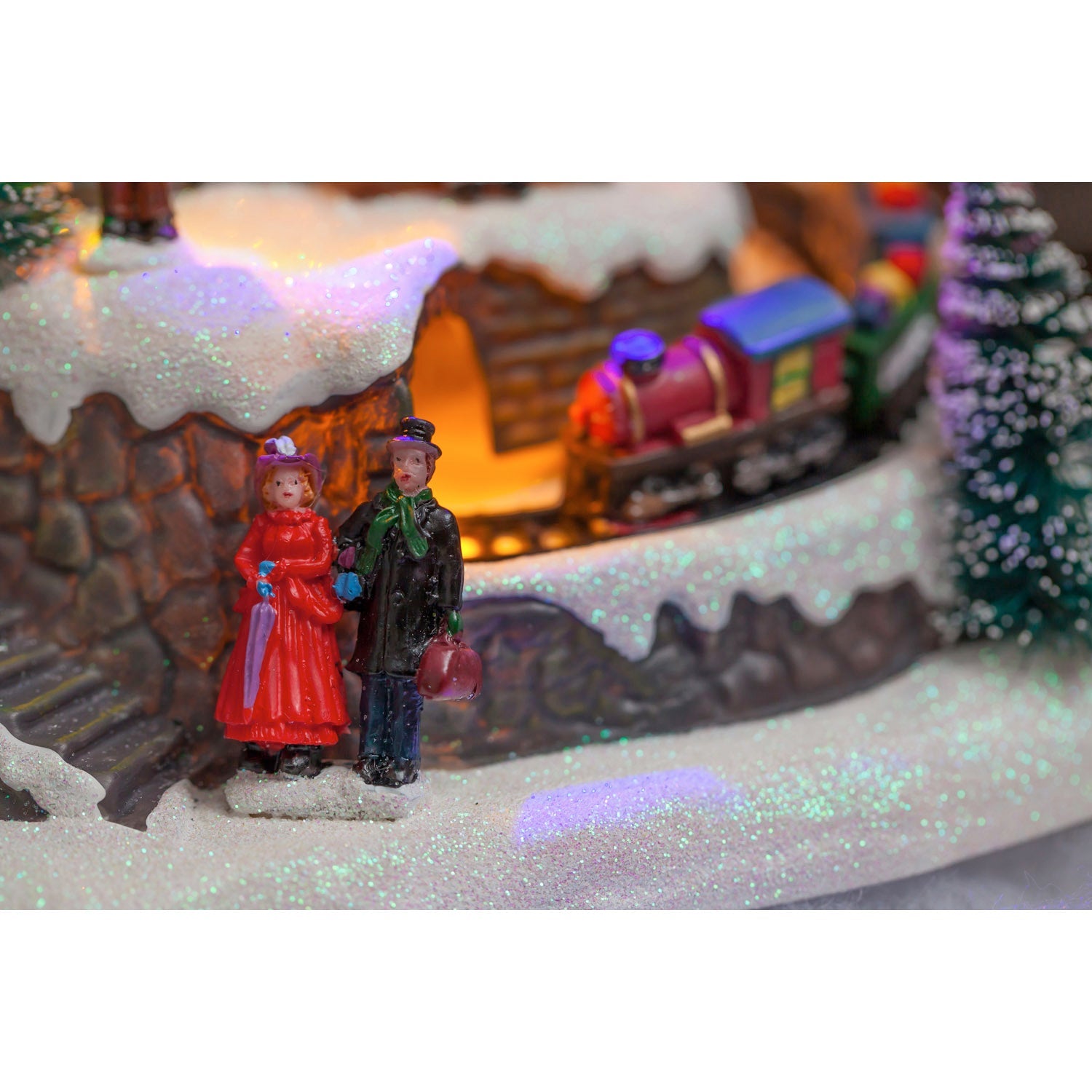 Close-up of the little red train coming out of the tunnel past a couple of carolers