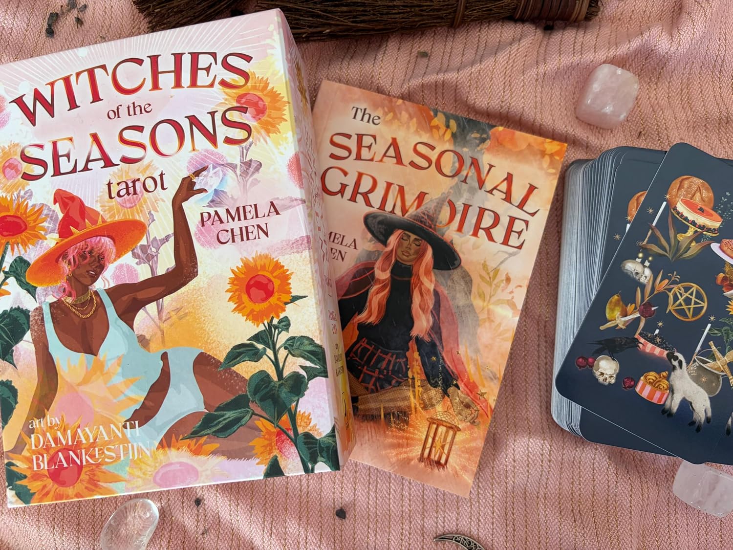 Witches of the Seasons Tarot box with The Seasonal Grimoire guidebook and a stack of navy cards on pink cloth