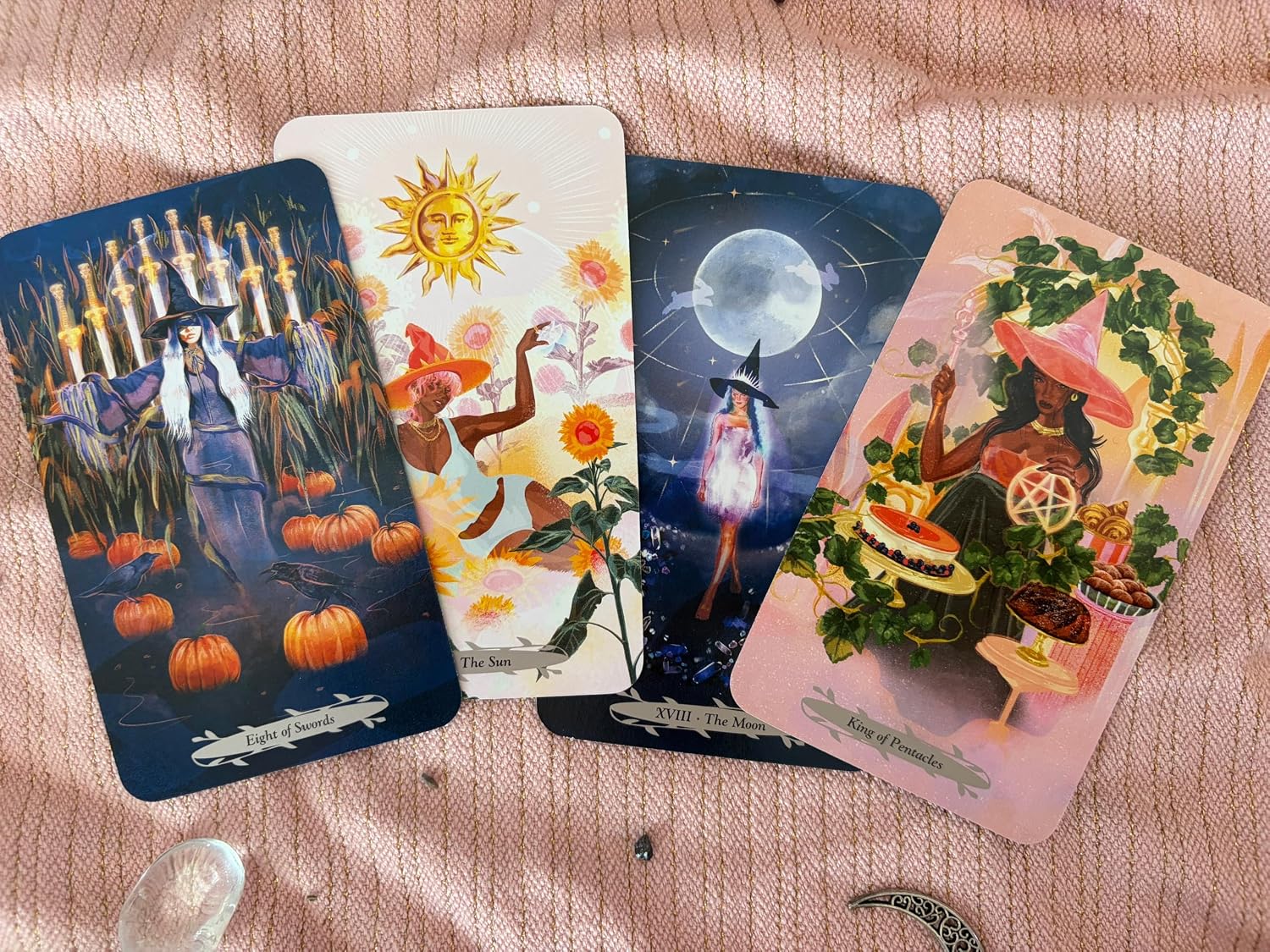 Eight of Swords, The Sun, The Moon and King of Pentacles cards from Witches of the Seasons Tarot on pink cloth