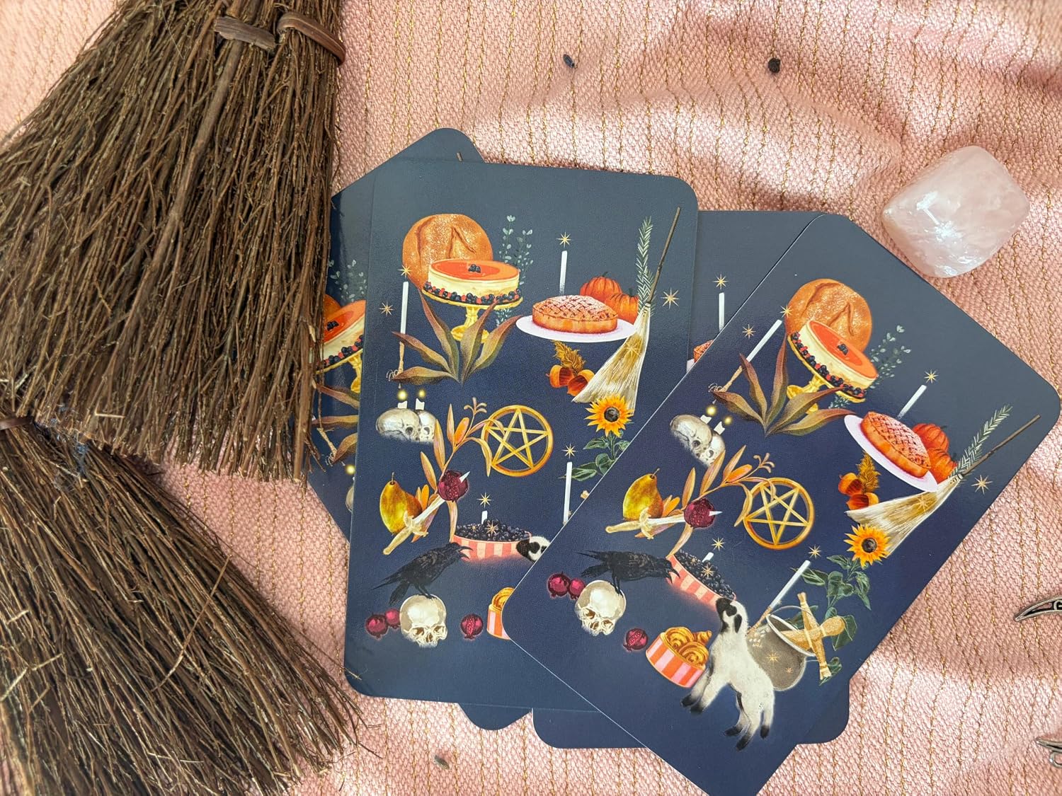 Witches of the Seasons Tarot card backs: navy art with pies, candles, a pentacle, skulls and a lamb, beside mini brooms