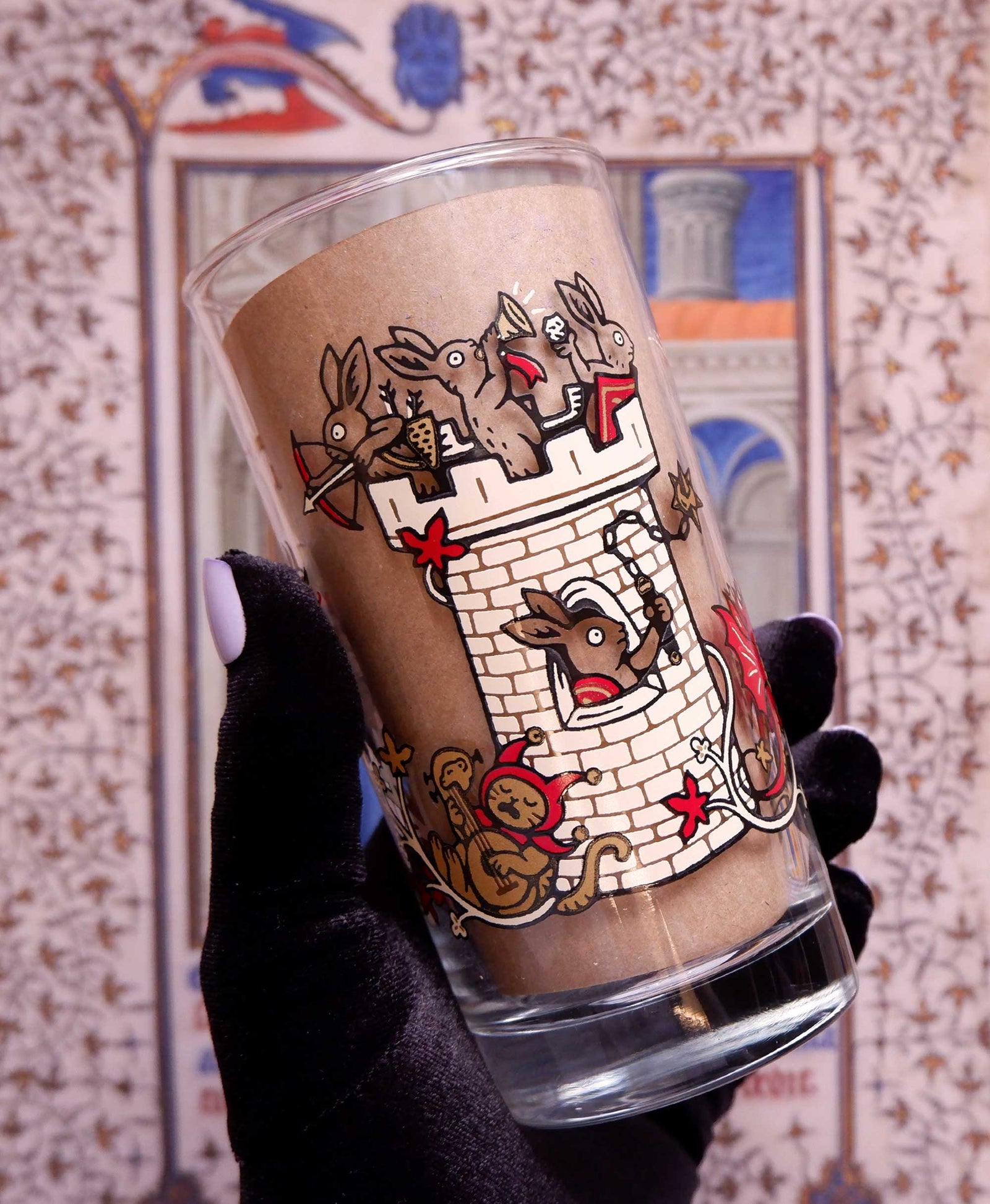 Glass with a castle design held by a gloved hand against a decorative background