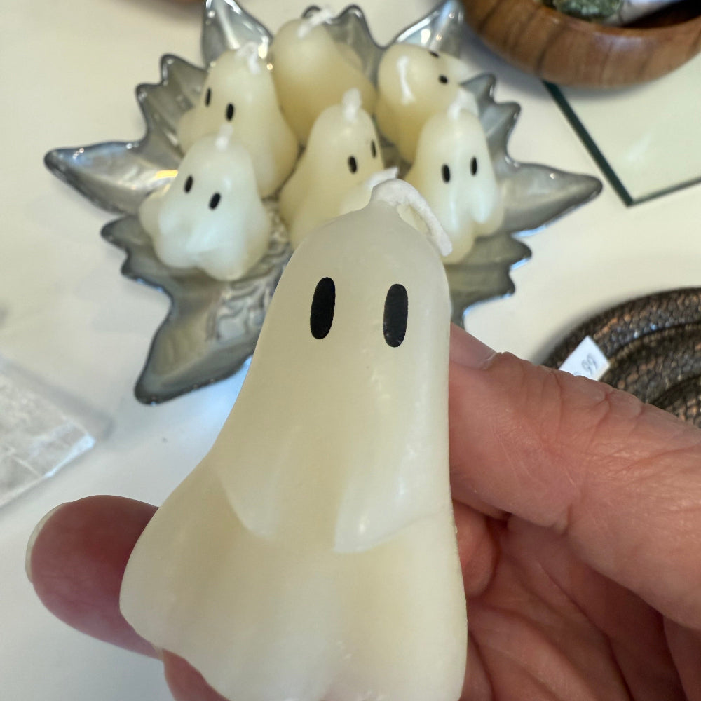 Hand holding a white ghost-shaped object with black dots on a tiled surface.