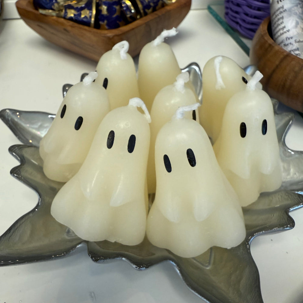 White ghost-shaped candles with black spots on a decorative stand.