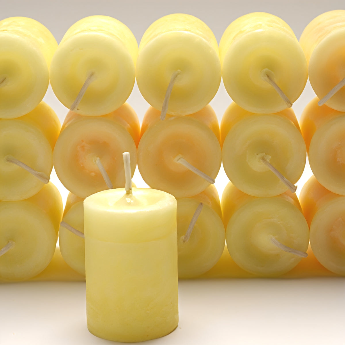 Pale yellow Happiness Power Votive candle in front of rows of stacked yellow votives