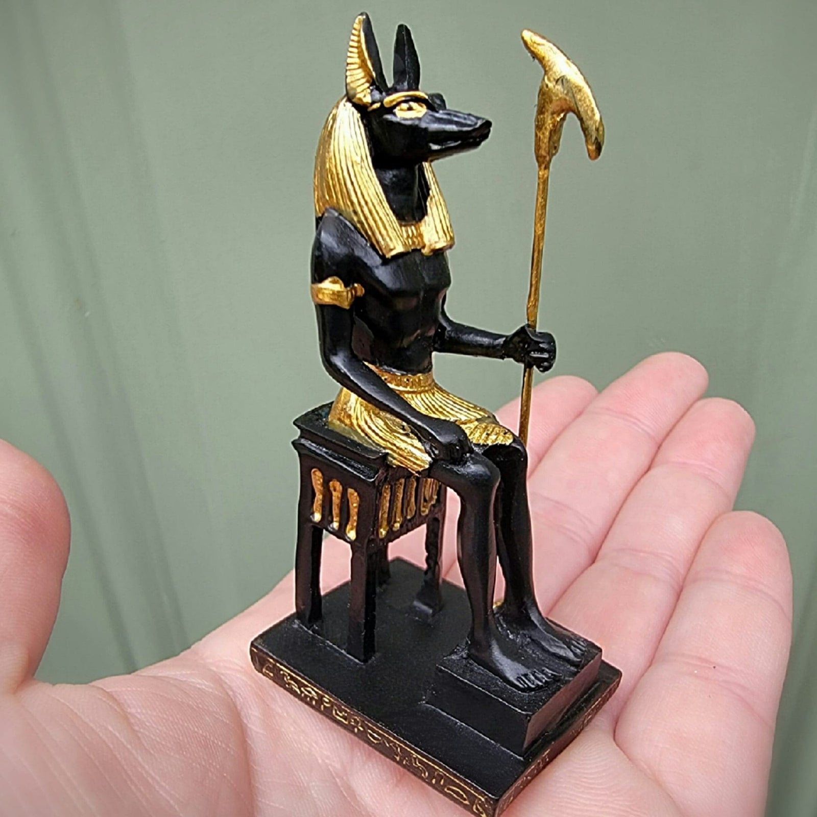 Black and gold Egyptian god statue held in a hand against a green background