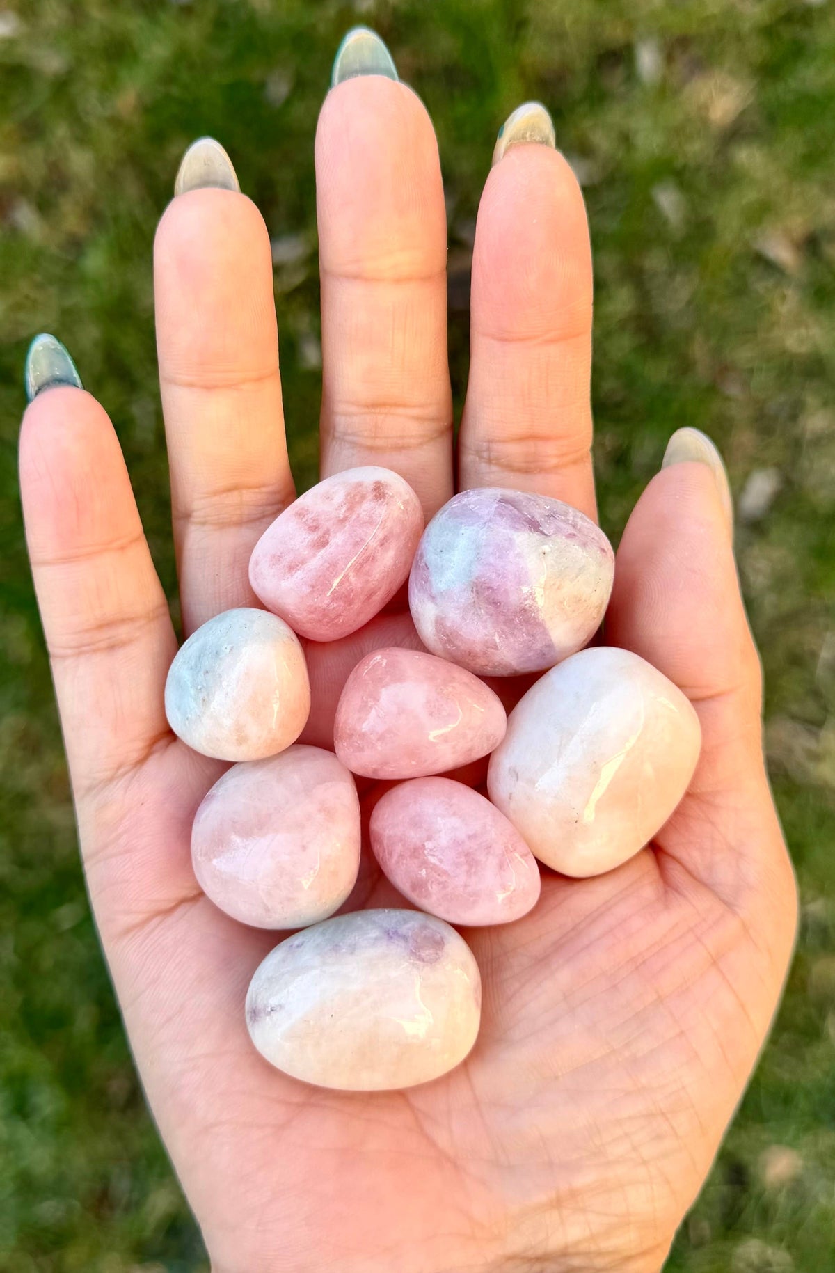 Hand holding pink marbled stones with a blurred grass background