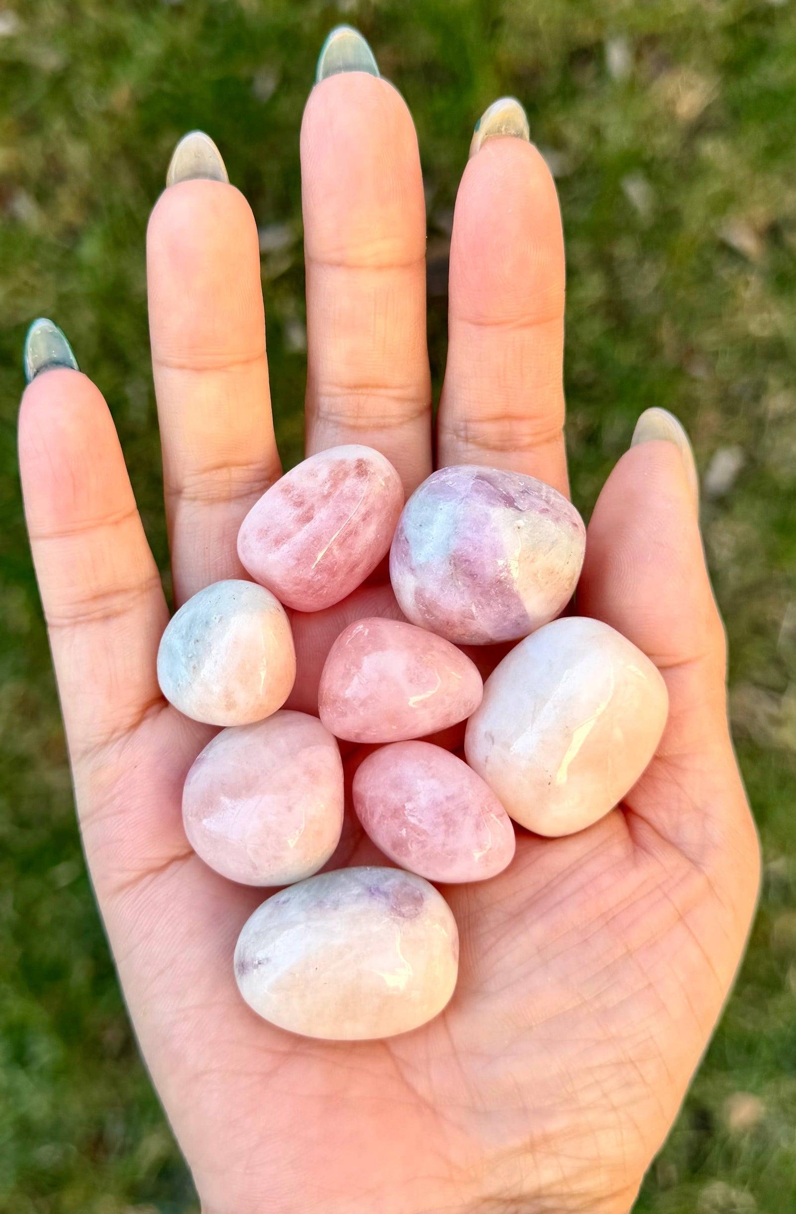 Hand holding pink marbled stones with a blurred grass background