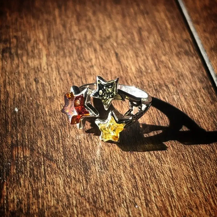 A silver-toned ring with three dangling star charms in red, green, and yellow, resting on a dark wooden surface.