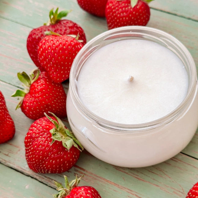 Jar of white candle with strawberries on a light green wooden surface