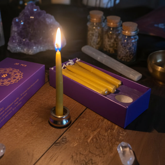 Lit yellow candle in front of a purple box with candles inside on a wooden surface