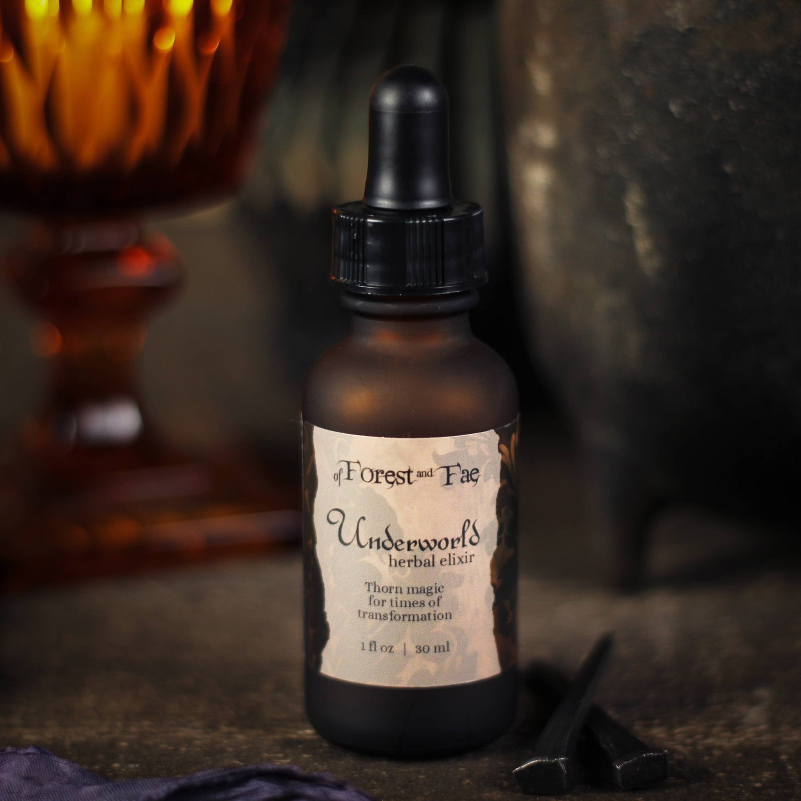 Underworld herbal elixir 1 fl oz amber dropper bottle with thorns beside it and a candle behind