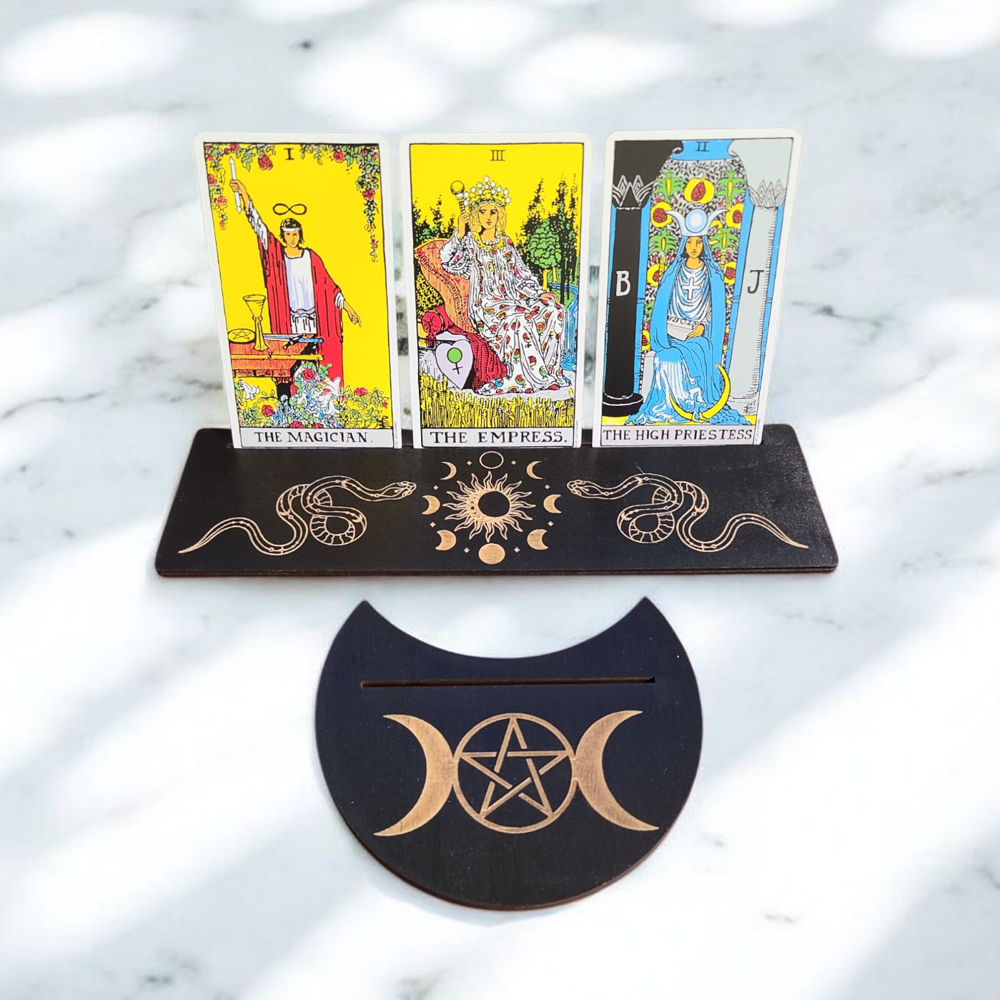 Three tarot cards on a stand with wiccan symbols on a marble surface