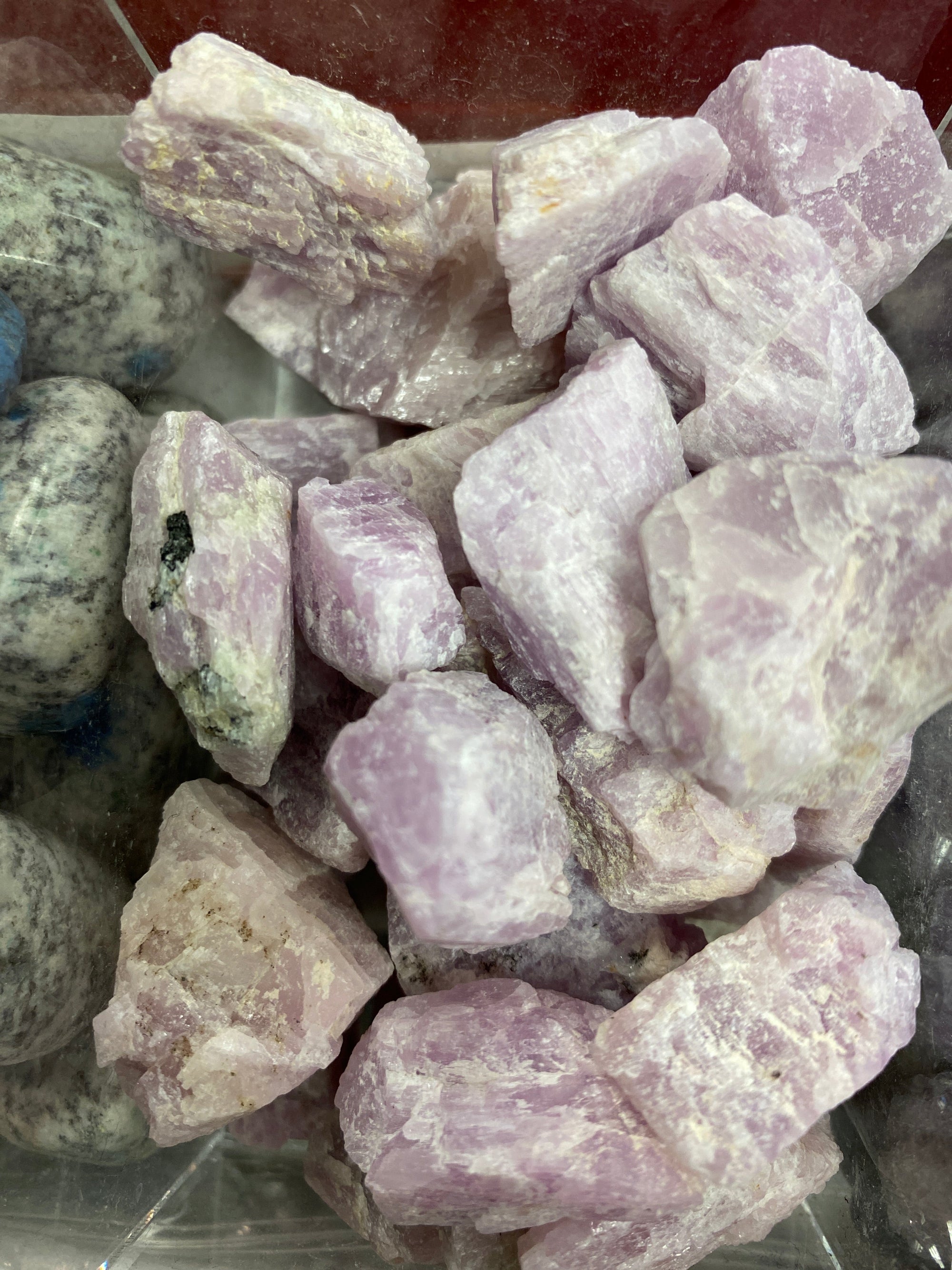 A collection of rough kunzite gemstones with varying shades of pink to purple and white, displayed in a tray.