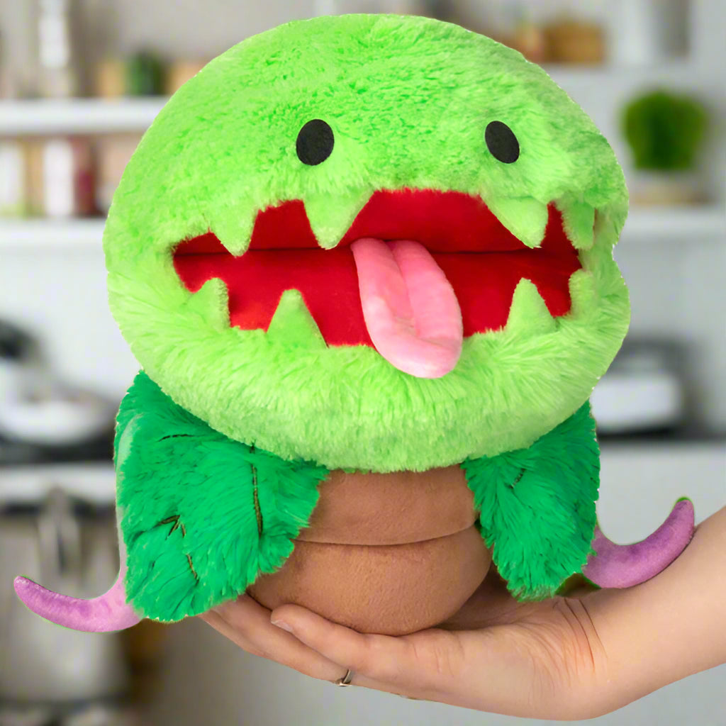 Green plush toy with a wide open mouth held in a hand on a white background