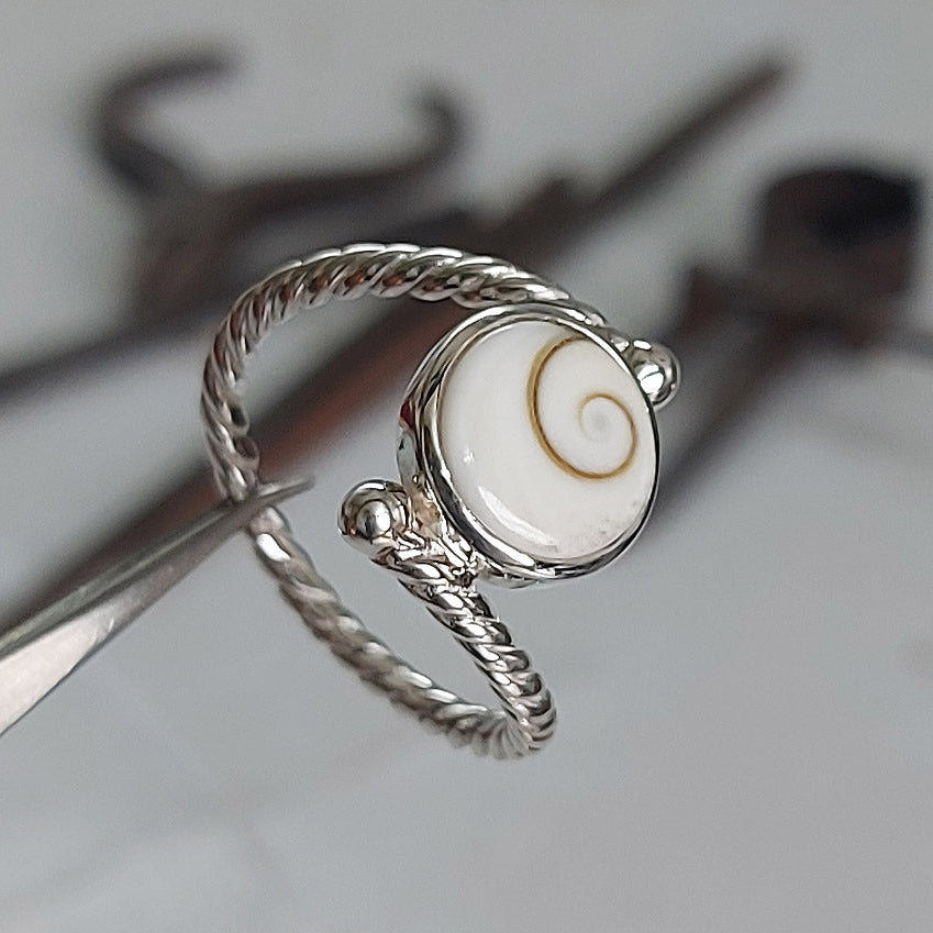 Silver ring with a white stone and gold spiral design on a blurred background