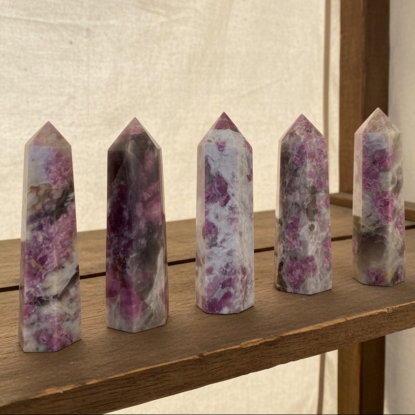 Set of six pink and gray crystal points on a light surface with green plants in the background
