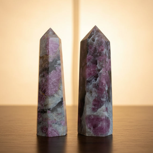 Two crystal sticks with pink and white patterns held in a hand, with green plants in the background.