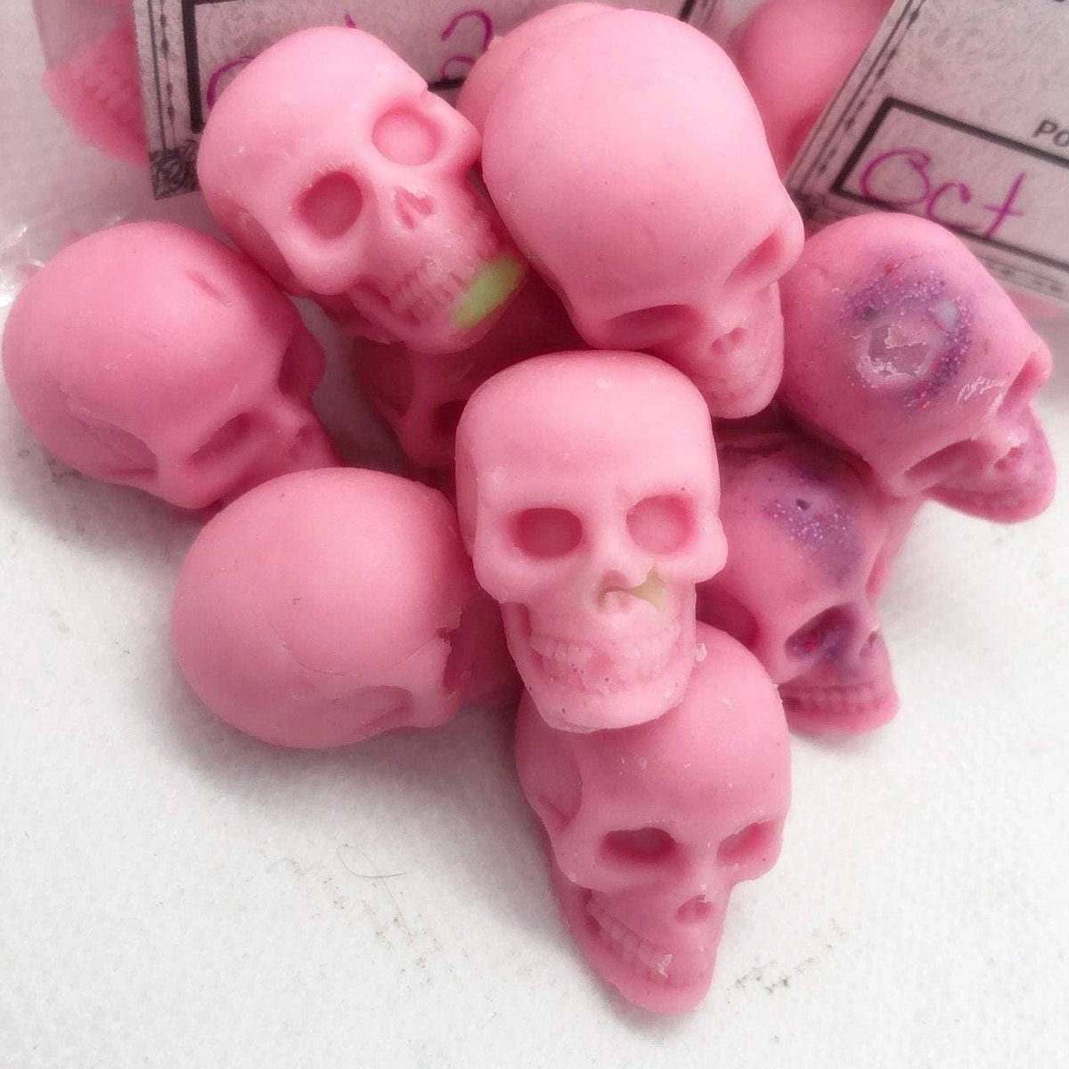 A collection of pink mini skull-shaped wax melts with labels indicating the product name and date.