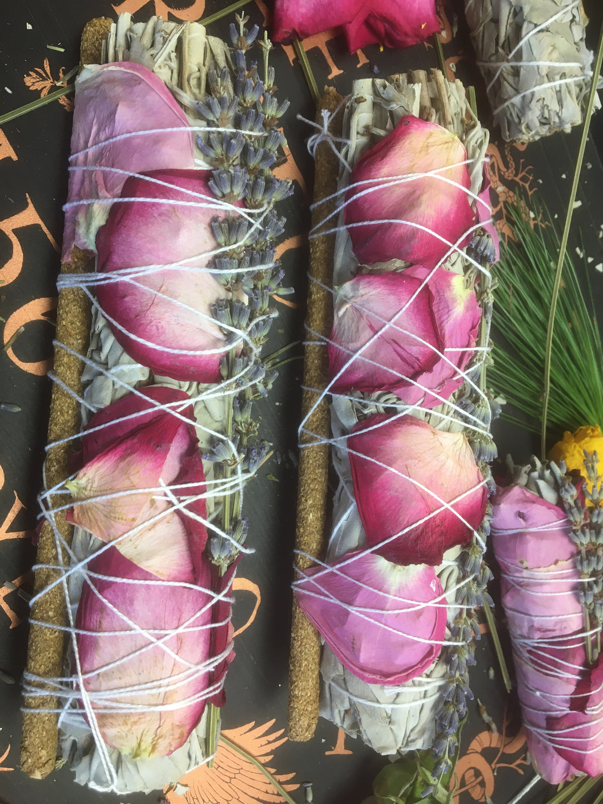 Hand-wrapped floral sage bundles with rose petals and cinnamon in front of an engraved Floral Sage Bundles sign